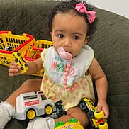 Isabella is registered to the contest to win money with this photo: toddler, child, toy, pacifier, pink_bow, couch, green_couch, yellow_toy, plastic_toys, white_shoes, baby_bib, indoor, playtime, curly_hair, sitting, young_child, cute, home, fun, colorful