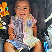 Enrique is registered to the contest to win money with this photo: baby, infant, child, smiling, car_seat, seat, toy, striped_clothing, pocket, happy, face, eyes, legs, hands, safety_harness, stroller, cute, portrait, button_up_shirt, canopy