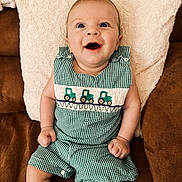 Matteo joined the competition — help win amazing prizes! baby, smiling, green_checkered_romper, embroidered_tractors, couch, brown_couch, white_pillow, cozy, happy, child, infant, cute, indoors, portrait, sitting, clothing, hands, legs, face, blue_eyes