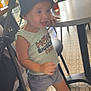 blue_crocs, bucket_hat, cafe, casual_clothing, chair, child, daylight, floor_tiles, hand_on_table, indoor, person, shoes, shorts, sleeveless_shirt, smiling, stroller, table, toddler, walking, window