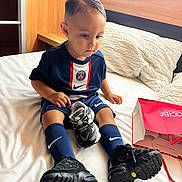 Kais participe au concours pour gagner de l'argent avec cette photo : toddler, child, bed, sneaker, shoes, socks, sportswear, nike, psg, clothing, indoor, pillow, shopping_bag, furniture, person, portrait, cute, serious, hair, floor