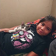 Xena joined the competition — help win amazing prizes! bedroom, blanket, cartoon_graphic, casual, child, comfort, cuddle, cute, gray_and_white_cat, indoor, kitten, lying_down, pillow, portrait, relax, resting, shirt, smile, wall, young_person
