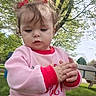 toddler, child, outdoor, grass, tree, pink_sweater, red_cuffs, curly_hair, hair_bows, hands, park, daylight, person, cute, young_child, nature, picnic_table, casual_clothing, expression, curiosity