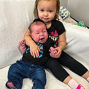 Realynn is registered to the contest to win money with this photo: baby, child, sibling, couch, clothing, black_shirt, blue_jeans, pink_socks, indoor, family, portrait, cute, hug, smile, expression, toddler, infant, home, soft_texture, person