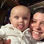 baby, tongue_out, white_hoodie, smiling_adult, nose_piercing, indoor, person, holding, face, child, cute, playful, portrait, infant, sitting, sleeve, hand, shelf, clothing, happy