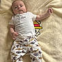 baby, infant, blanket, lying_down, white_shirt, printed_pants, superheroes, soft_texture, cartoon_design, child, cute, indoors, casual_clothing, socks, person, young_child, comfortable, resting, portrait, looking_at_camera