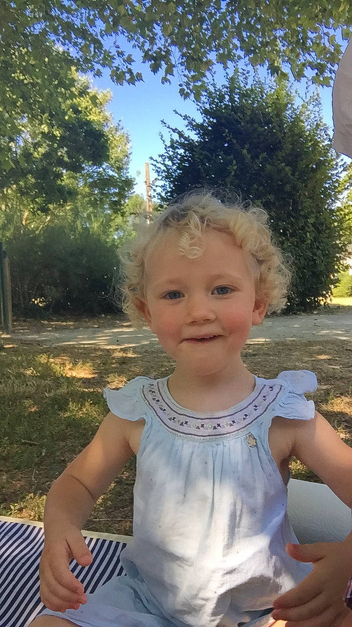 Charline participe au concours pour gagner de l'argent avec cette photo : active_tank, baby, baby_toddler_clothing, blond, child, day_dress, joy, mouth, outdoor_furniture, overall, person, sleeveless_shirt, summer, sunlight, toddler, yard