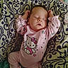 baby, infant, sleeping, pink_outfit, onesie, hello_kitty, cushion, patterned_fabric, portrait, indoors, sitting, arms_raised, closed_eyes, peaceful, nursery, pacifier, furniture, textile, cute, child