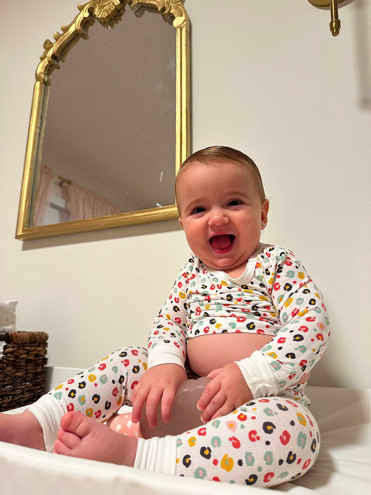 Lucia is registered to the contest to win money with this photo: baby, child, smiling, pajamas, colorful, toy, sitting, indoor, mirror, gold_frame, happy, face, hands, feet, furniture, wall, home, decor, clothing, person