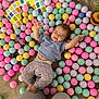 Lucia joined the competition — help win amazing prizes! baby, child, colorful_balls, ball_pit, pastel_colors, toys, floor, cushion, person, playtime, happy, smiling, clothing, pants, tshirt, barefoot, indoor, cute, fun, family