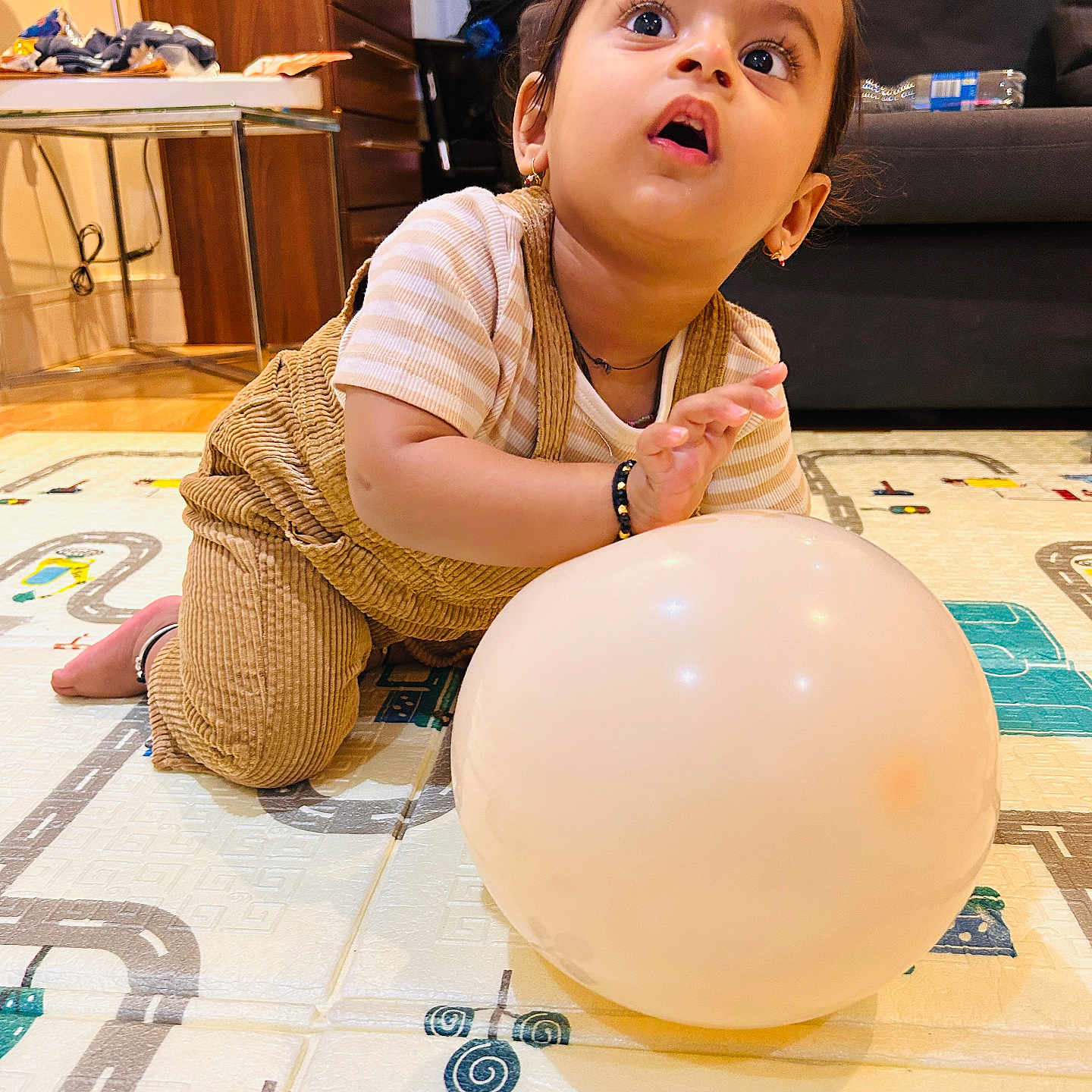 Vihaan is registered to the contest to win money with this photo: balloon, bracelet, candid, child, curious, curtains, cute, earrings, expression, floor_mat, home, indoors, lamp, overalls, play_mat, sofa, striped_shirt, toddler, toy, wooden_furniture