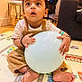 toddler, child, balloon, indoor, playmat, curious, sitting, clothing, corduroy, bracelet, earrings, living_room, carpet, toy, expression, person, floor, foot, hand, furniture