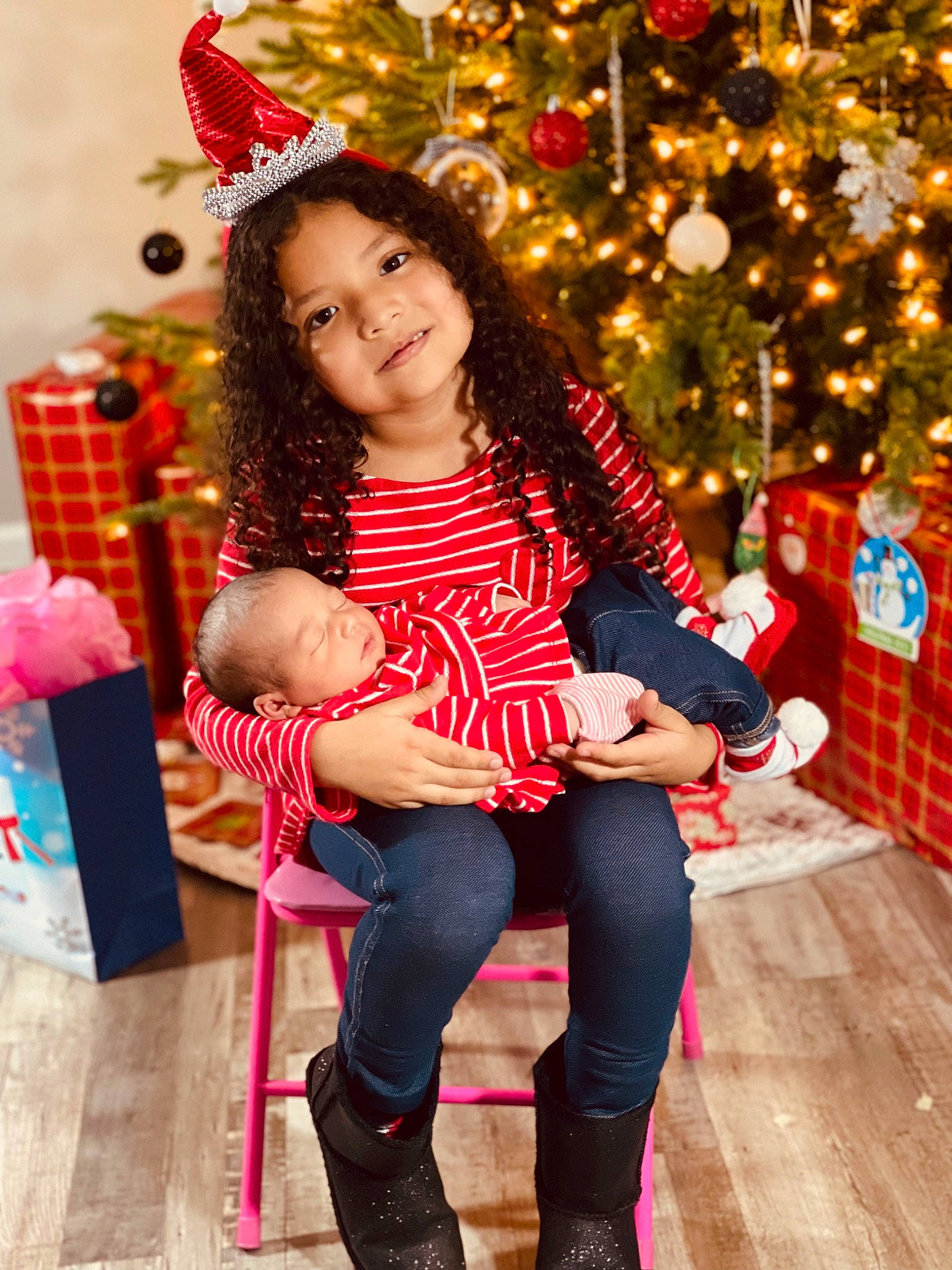 Adalynn Rose is registered to the contest to win money with this photo: chair, child, christmas, christmas_decoration, christmas_ornament, christmas_tree, event, facial_expression, fun, happy, head, holiday, human_body, joy, ornament, person, pink, red, smile, sock