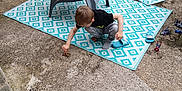 Enzo a rejoint le concours — aidez-le/la à gagner de superbes lots ! child, boy, plastic_chair, outdoor, rug, concrete, slippers, toys, play, crouching, curious, wooden_fence, casual, daylight, footwear, pattern, concrete_floor, plastic, backyard, exploration