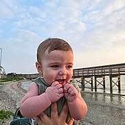 Theo is registered to the contest to win money with this photo: baby, beach, child, clouds, cute, hand, happy, holding, infant, nature, outdoor, person, pier, portrait, shore, sky, smiling, summer, water, wood