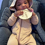 Ramari Roberson is registered to the contest to win money with this photo: baby, child, hoodie, onesie, infant, cushion, seat, wooden_plaque, chewing, hands, face, eyes, clothing, indoor, cute, portrait, baby_seat, comfortable, sitting, young_child