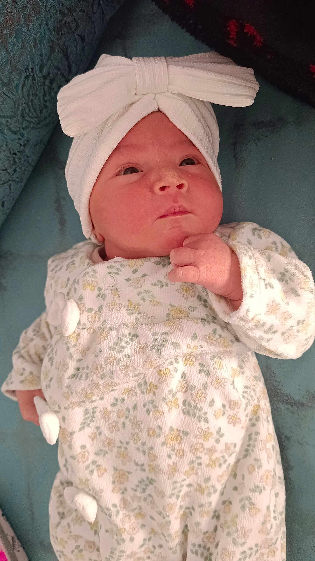 Kaïna participe au concours pour gagner de l'argent avec cette photo : baby, infant, headband, bow, onesie, floral_pattern, hand, face, skin, clothing, lying_down, cute, expression, newborn, child, indoors, soft_texture, blanket, resting, portrait