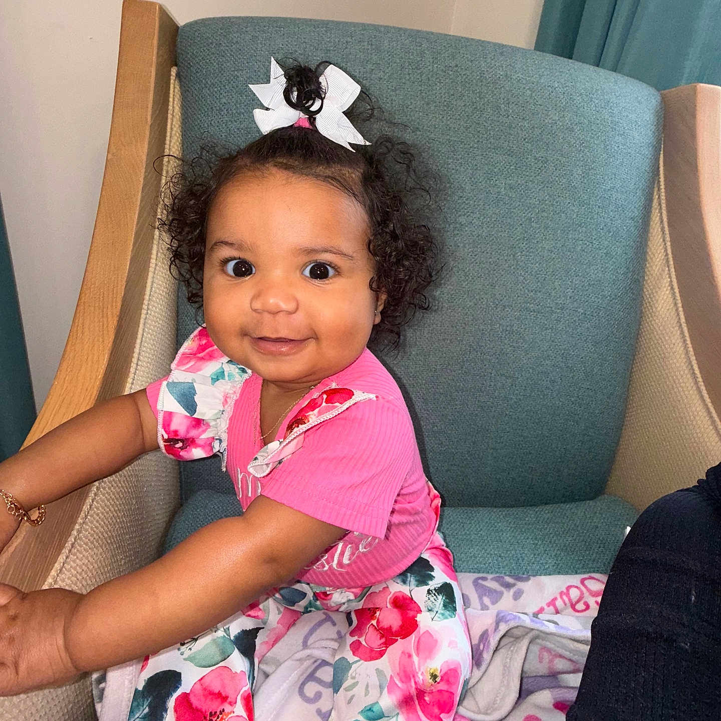 Saniya joined the competition — help win amazing prizes! blanket, bow, bright_eyes, chair, child, cozy, curly_hair, cute, floral_pants, happy, home, indoor, person, pink_clothing, playful, portrait, sitting, smiling, toddler, young_child