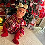 baby, child, plaid_dress, red_tights, headband, bow, christmas_tree, ornaments, holiday_decor, plush_toy, elephant_toy, carpet, festive, indoor, cute, portrait, celebration, holiday, seasonal, smiling