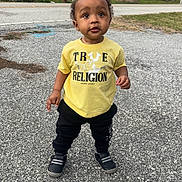 Amir Mcintosh is registered to the contest to win money with this photo: toddler, child, standing, yellow_shirt, black_pants, outdoor, pavement, suburban, house, trees, curious, person, footwear, grass, daytime, casual_clothing, sidewalk, young_child, urban, nature