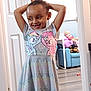 Bella is registered to the contest to win money with this photo: child, smiling, dress, animated_characters, indoor, doorway, stuffed_toys, chair, floor, happy, person, playful, room, furniture, toy, patterned_clothing, hair_bun, missing_teeth, casual_wear, home