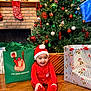 baby, child, christmas_tree, christmas_decorations, christmas_gifts, festive_clothing, santa_hat, red_outfit, smiling, holiday, indoor, fireplace, stocking, wooden_floor, present_bag, ornaments, teddy_bear_wrapping, green_wrapping_paper, happy, celebration