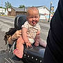 baby, child, motorcycle, outdoor, funny_face, tongue_out, seat, person, hand, clothing, bracelet, road, building, sky, daytime, urban, humor, cute, expression, holding