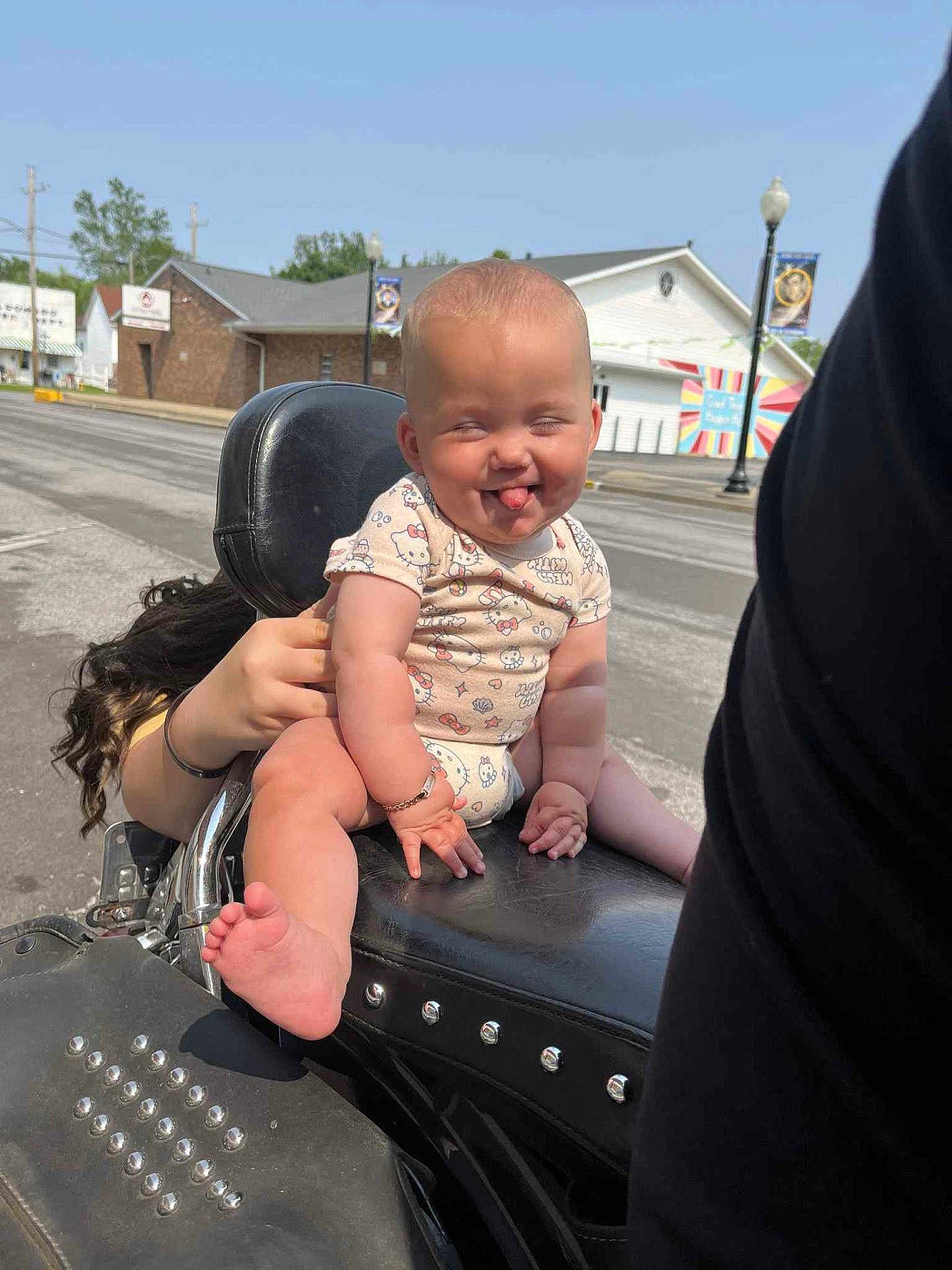 Zyalani joined the competition — help win amazing prizes! baby, child, motorcycle, outdoor, funny_face, tongue_out, seat, person, hand, clothing, bracelet, road, building, sky, daytime, urban, humor, cute, expression, holding