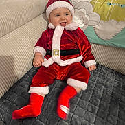 Eden a rejoint le concours — aidez-le/la à gagner de superbes lots ! baby, child, santa_claus_outfit, red_clothing, smiling, couch, blanket, home_interior, holiday, festive, cute, infant, hat, plush, happy, sitting, indoor, person, face, sock