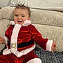 baby, child, smiling, red_clothing, santa_outfit, couch, blanket, indoor, happy, fur_trim, holiday, festive, person, portrait, young_child, cozy, seated, cute, hair, cheerful