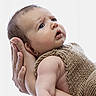 baby, infant, hands, knitted_clothing, brown_outfit, portrait, closeup, skin, expression, curious, adult_hands, supporting, soft_light, studio, newborn, child, human, cute, face, baby_girl