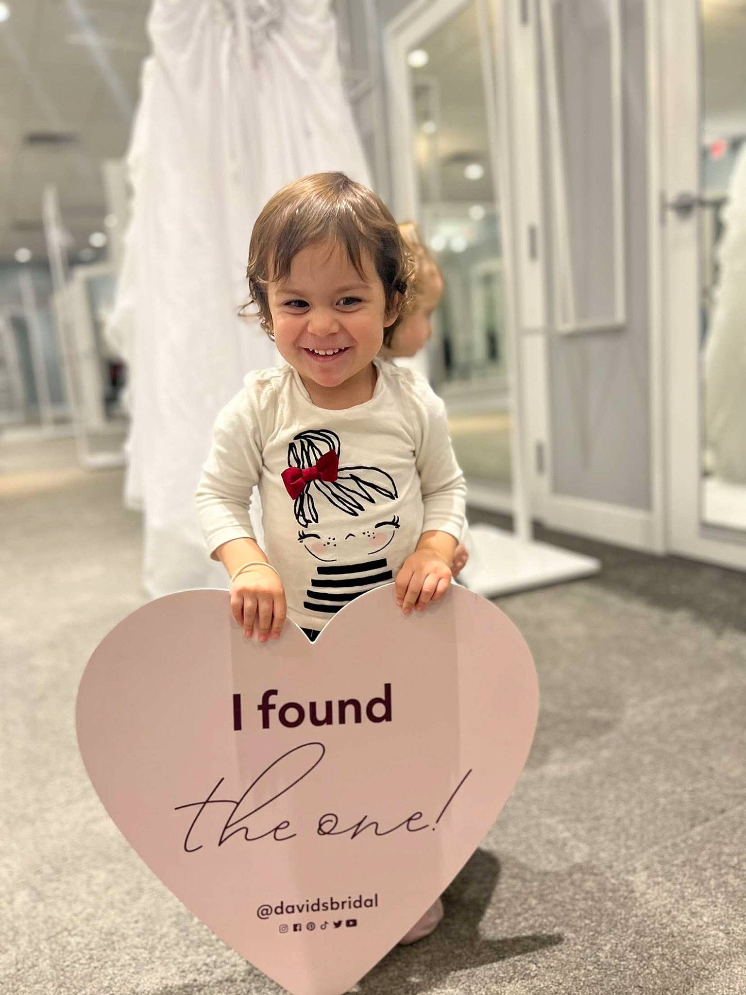 Ariella is registered to the contest to win money with this photo: baby, baby_toddler_clothing, blond, child, dress, event, flooring, font, formal_wear, fun, happy, joy, logo, people, person, room, sleeve, smile, standing, t_shirt