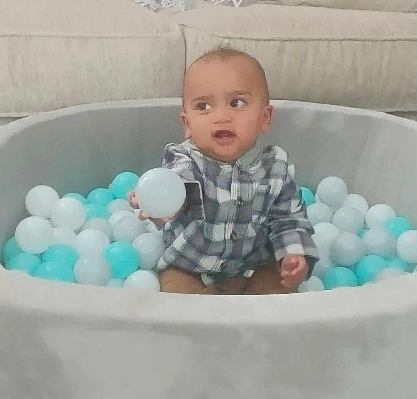 Kairo is registered to the contest to win money with this photo: toddler, child, ball_pit, plastic_balls, indoor, playtime, curious, checkered_shirt, seated, toy, colorful, young_child, smiling, fun, home, couch, soft_furniture, casual_clothing, baby, play