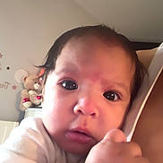 Julieth is registered to the contest to win money with this photo: baby, infant, child, portrait, close_up, face, wide_eyes, looking_at_camera, indoor, bedroom, white_clothing, hand, gripping, strap, bracelet, toys, stuffed_animal, wall_decor, natural_light, candid