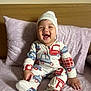 baby, child, smiling, pajamas, hat, bed, pillow, wooden_headboard, indoor, person, happy, sitting, cute, infant, cozy, blanket, sleepwear, expression, portrait, young
