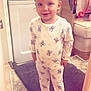 appliance, baby, carpet, child, cozy, cute, floor, footwear, home, indoor, pajamas, person, pink_shoes, pony_tail, rainbow, rug, smiling, standing, toddler, unicorn