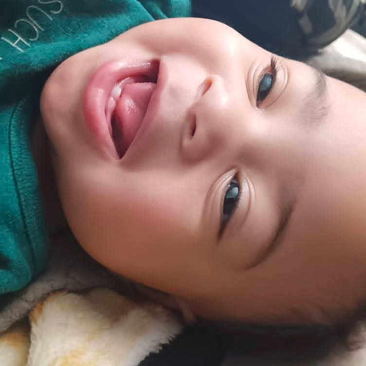 Lanyiah is registered to the contest to win money with this photo: baby, blanket, child, closeup, cozy, cute, expression, eyes, face, green_shirt, happy, indoors, infant, laughing, lying_down, mouth, person, skin, smiling, tongue