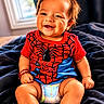 baby, smiling, child, diaper, red_shirt, spiderman, indoor, blanket, happy, cute, toddler, sitting, hair, face, person, portrait, skin, clothing, window, bracelet