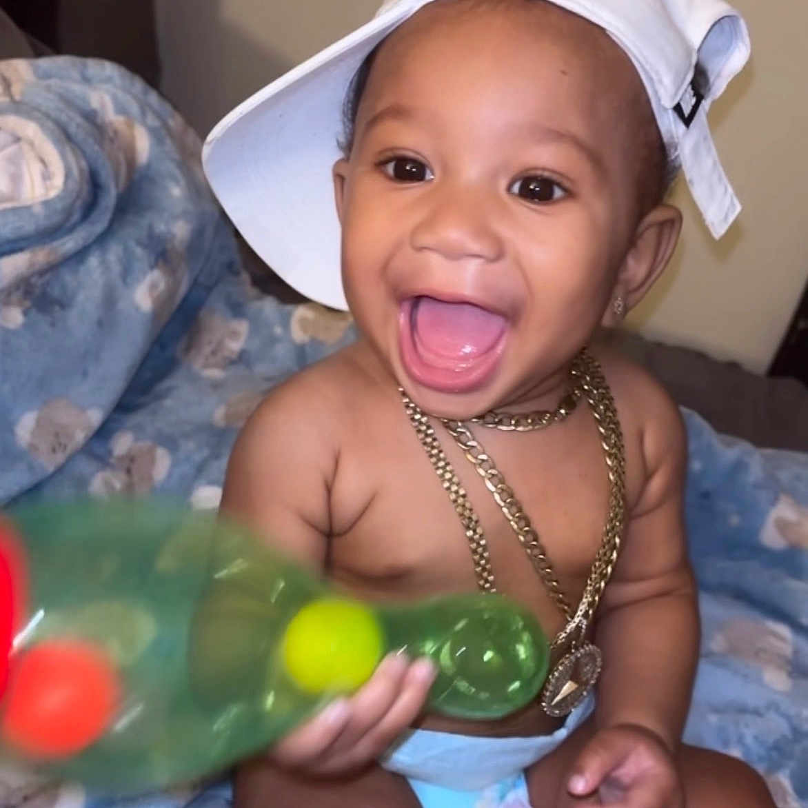 Darrian is registered to the contest to win money with this photo: baby, child, smiling, hat, cap, gold_chain, diaper, blanket, toy, pacifier, indoor, cute, happy, infant, portrait, human, toddler, sitting, playful, accessory