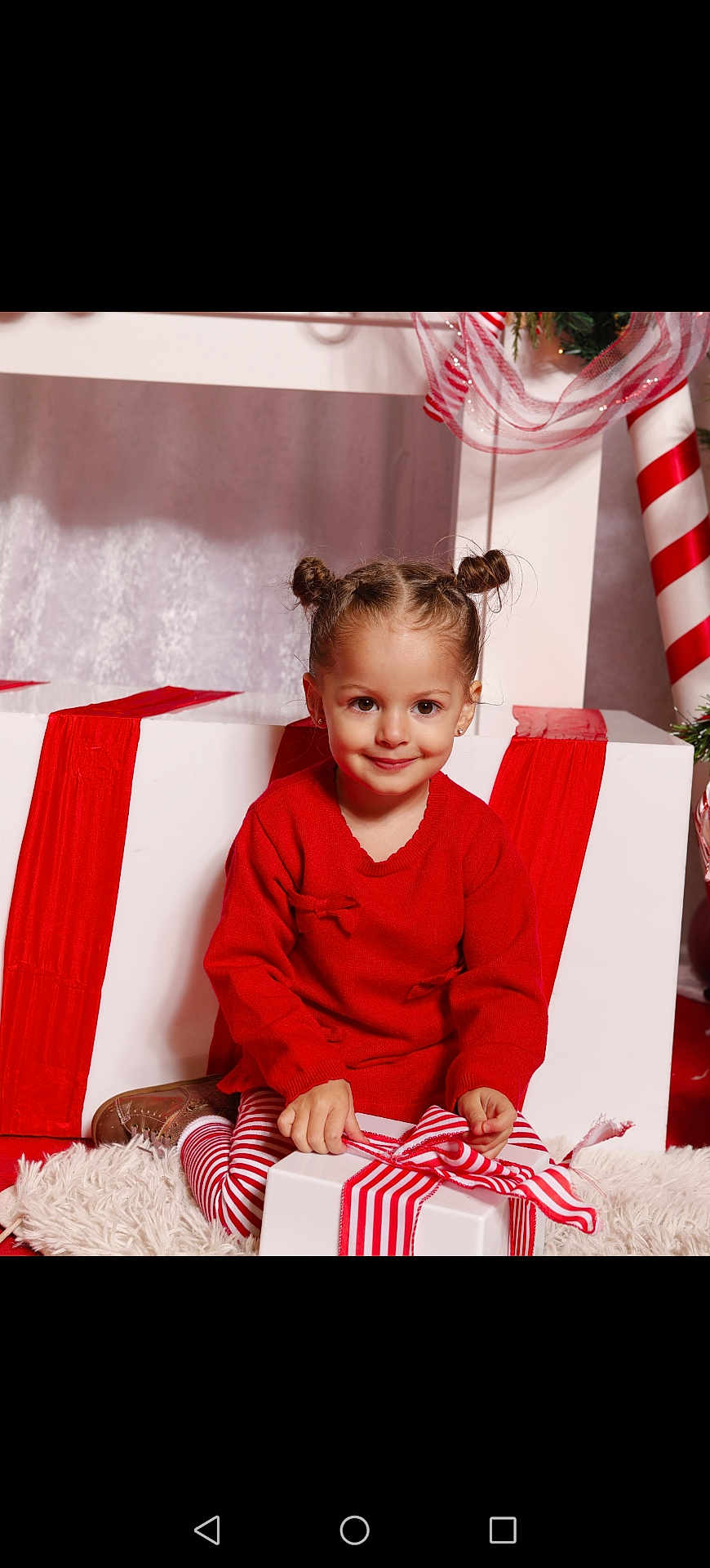 Saona participe au concours pour gagner de l'argent avec cette photo : child, girl, smile, red_sweater, striped_leggings, gift_box, ribbon, holiday, christmas, decorations, present, festive, hair_buns, carpet, indoor, cute, portrait, happy, celebration, seasonal
