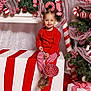 toddler, child, smiling, red_sweater, striped_leggings, lollipop, christmas_decorations, candy_cane, gift_box, holiday_theme, festive, christmas_tree, ribbon, greenery, indoor, portrait, cute, holiday_season, red_and_white, happy
