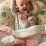 baby, smiling, blanket, plush_toy, playpen, pajamas, pacifier, infant, cute, sleeping_area, face, happy, child, soft_toys, comfort, indoors, cushion, colorful, patterned, cozy