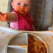 Sunny joined the competition — help win amazing prizes! toddler, child, high_chair, messy, spaghetti_sauce, food, plate, pink_clothing, bib, reaching_hand, face, blue_eyes, hair, indoor, feeding, meal_time, curious, expression, baby_food, seat