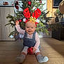 Capucine a rejoint le concours — aidez-le/la à gagner de superbes lots ! baby, child, christmas_tree, reindeer_antlers, red_ornament, smiling, holiday, festive, decorations, indoor, floor, wooden_floor, cute, happy, christmas_lights, blue_eyes, clothing, overalls, socks, seasonal