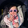 airbag_label, baby, car_seat, child, closeup, clothing, cute, harness, infant, onesie, pink_bib, pink_sunglasses, portrait, safety_strap, shadow, smile, stroller, sunglasses, sunlight, tongue_out