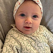 Margaux a rejoint le concours — aidez-le/la à gagner de superbes lots ! baby, blanket, blue_eyes, cheeks, child, close_up, date_display, eyelashes, face, grey_background, headband, heart_pattern, infant, onesie, patterned_clothing, portrait, screenshot, smile, soft_lighting, zipper