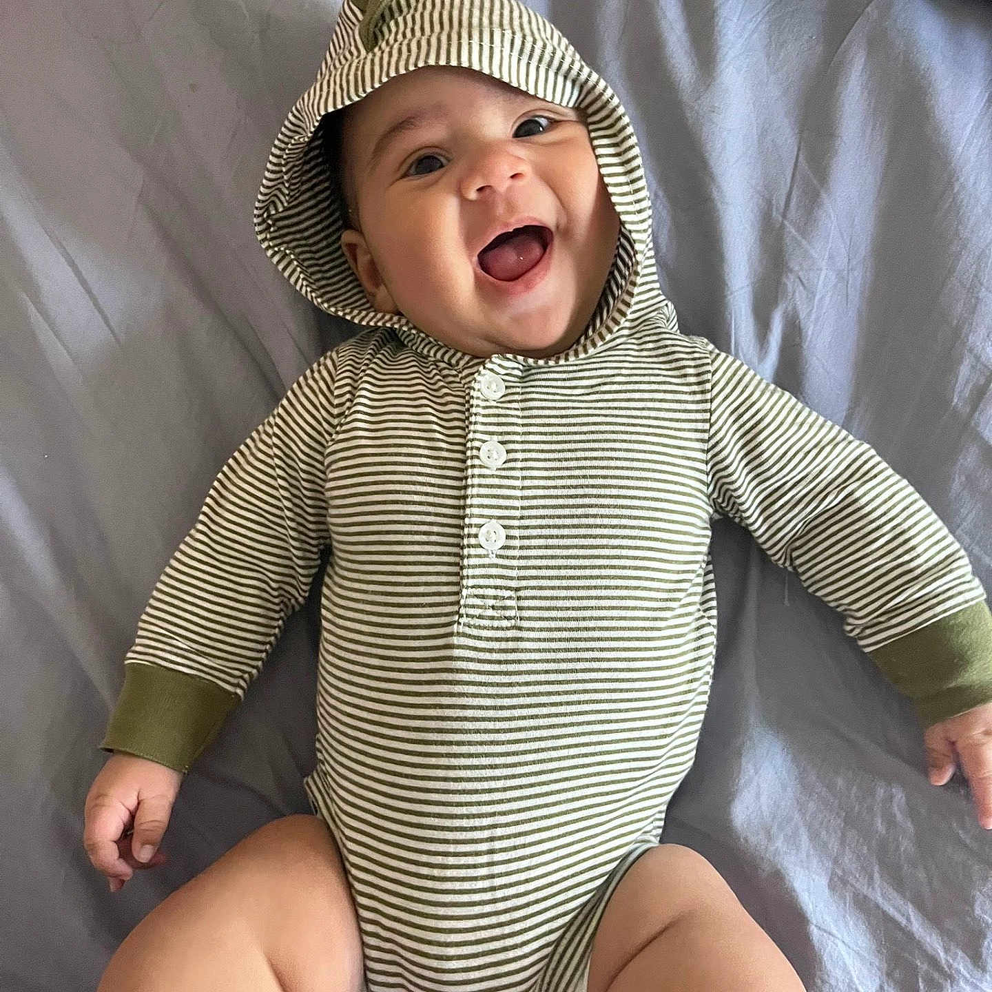Kaydenn is registered to the contest to win money with this photo: baby, infant, smiling, happy, hoodie, striped_clothing, onesie, bed, blanket, child, cute, chubby_legs, lying_down, portrait, indoor, person, face, head, young_child, joy