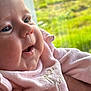 baby, close_up, face, smile, pink_clothing, chubby_cheeks, hand, soft_texture, portrait, infant, outdoor_background, greenery, happy, cute, child, skin, eyes, mouth, holding, person