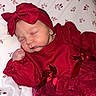 newborn, baby, sleeping, red_outfit, headband, bow, blanket, floral_pattern, cute, infant, portrait, closeup, soft_lighting, indoors, peaceful, baby_clothes, baby_girl, fabric, texture, resting