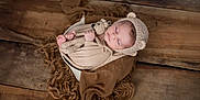 Lenzo a rejoint le concours — aidez-le/la à gagner de superbes lots ! newborn, baby, sleeping, knitted_hat, crocheted_toy, teddy_bear, wrapped_baby, bowl, brown_blanket, wooden_floor, peaceful, cute, infant, soft_texture, cozy, portrait, child, indoors, warm_colors, resting